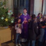 Lucy , le père Pierre Belhache, et les enfants tenant chacun leur personnage, à côté de la crèche